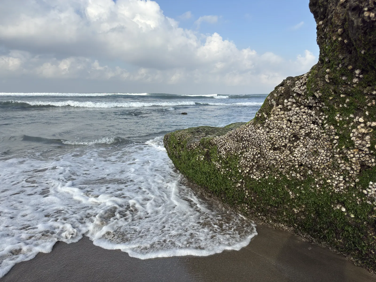 Waves breaking against a mossy rock on Canggu beach